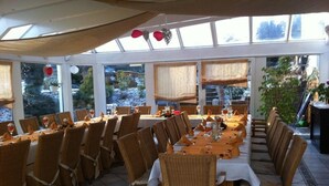 A restaurant with long tables, wicker chairs, and a view of a waterfall. - Hotel am Salzberg (Philippsthal)