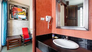 Ein Badezimmer mit roter Wand, schwarzem Waschtisch, weißem Waschbecken, einem roten Stuhl und einem gerahmten Kunstwerk.