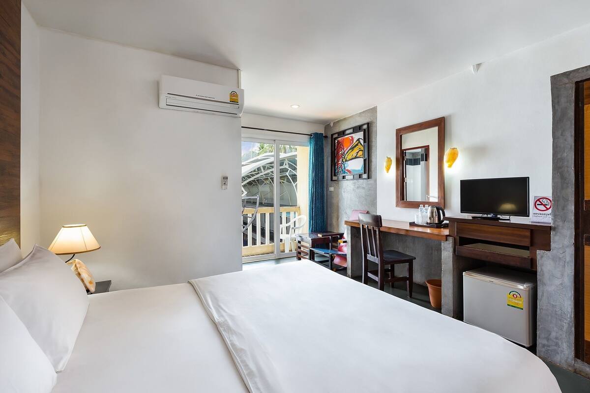 A hotel room with a bed, desk, TV, and a small refrigerator.