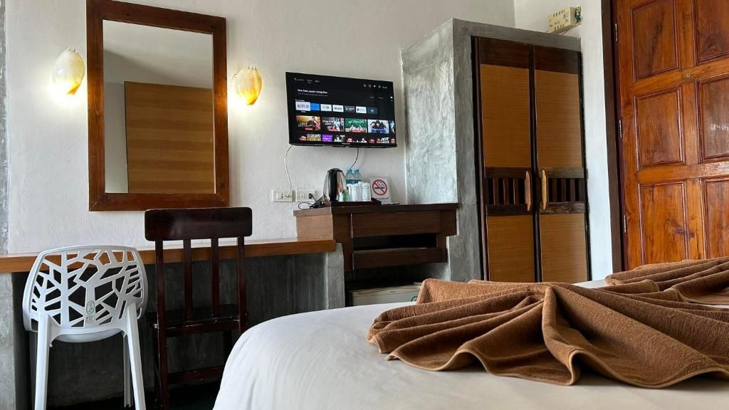 A hotel room with a bed, a desk with a chair, a television mounted on the wall, and a wardrobe.