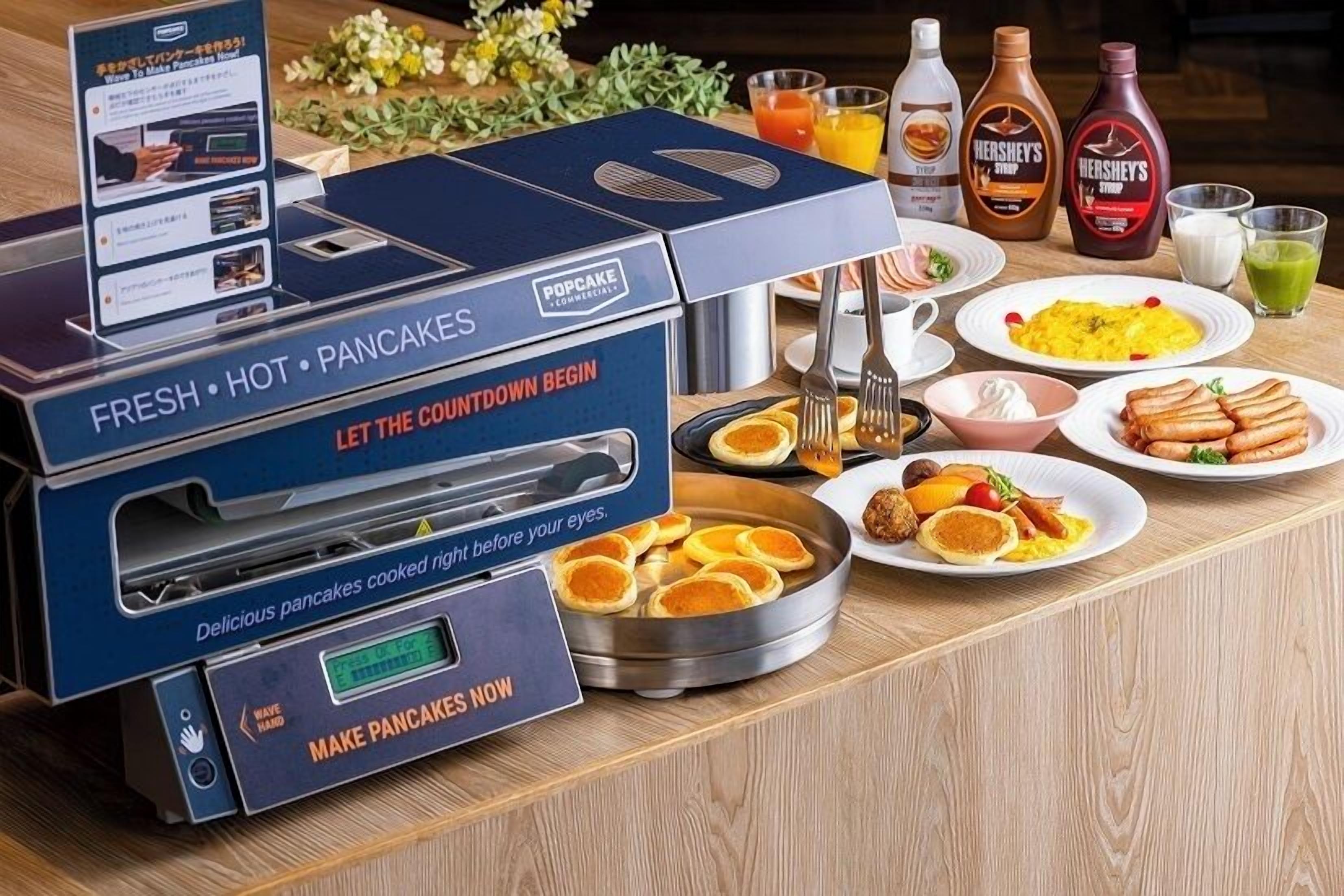 Un buffet pour le petit-déjeuner comprenant une machine à crêpes, des assiettes remplies de nourriture et diverses boissons.