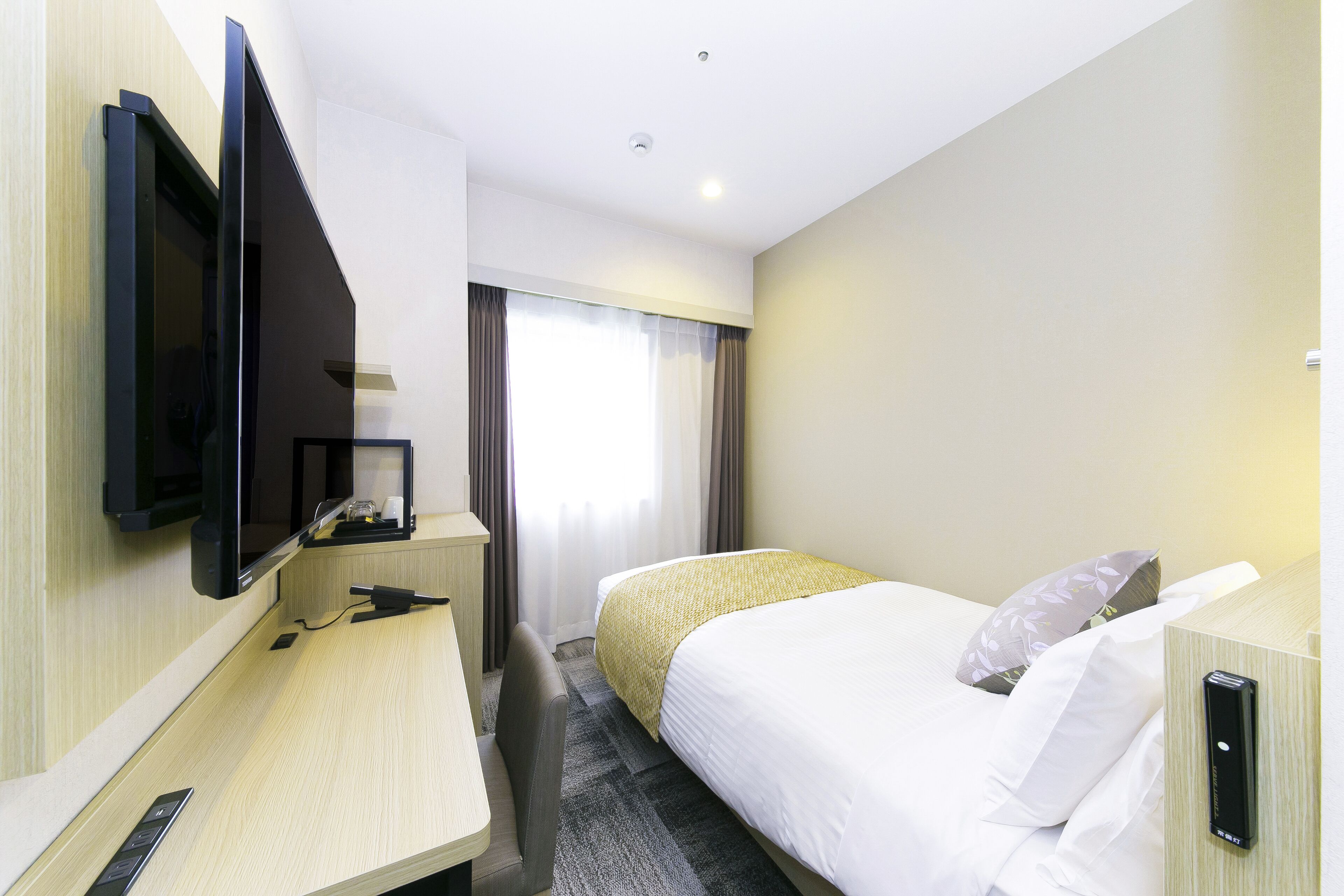 Habitación de hotel con cama, escritorio, televisor montado en la pared y ventana con cortinas.