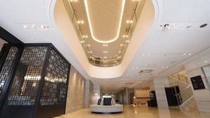 A modern hotel lobby with a central seating area, a high ceiling with recessed lighting, and a traditional decorative screen on the left. - Art Hotel Oita (Oita)