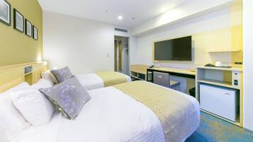 A hotel room with two beds, a desk, a television, and a mini-fridge.