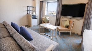 A hotel room with a sofa, a small table, a TV, a chair, and a mini-fridge. - Art Hotel Oita (Oita)