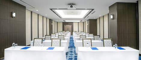 A conference room with rows of tables, a blue carpet, and a modern ceiling design.