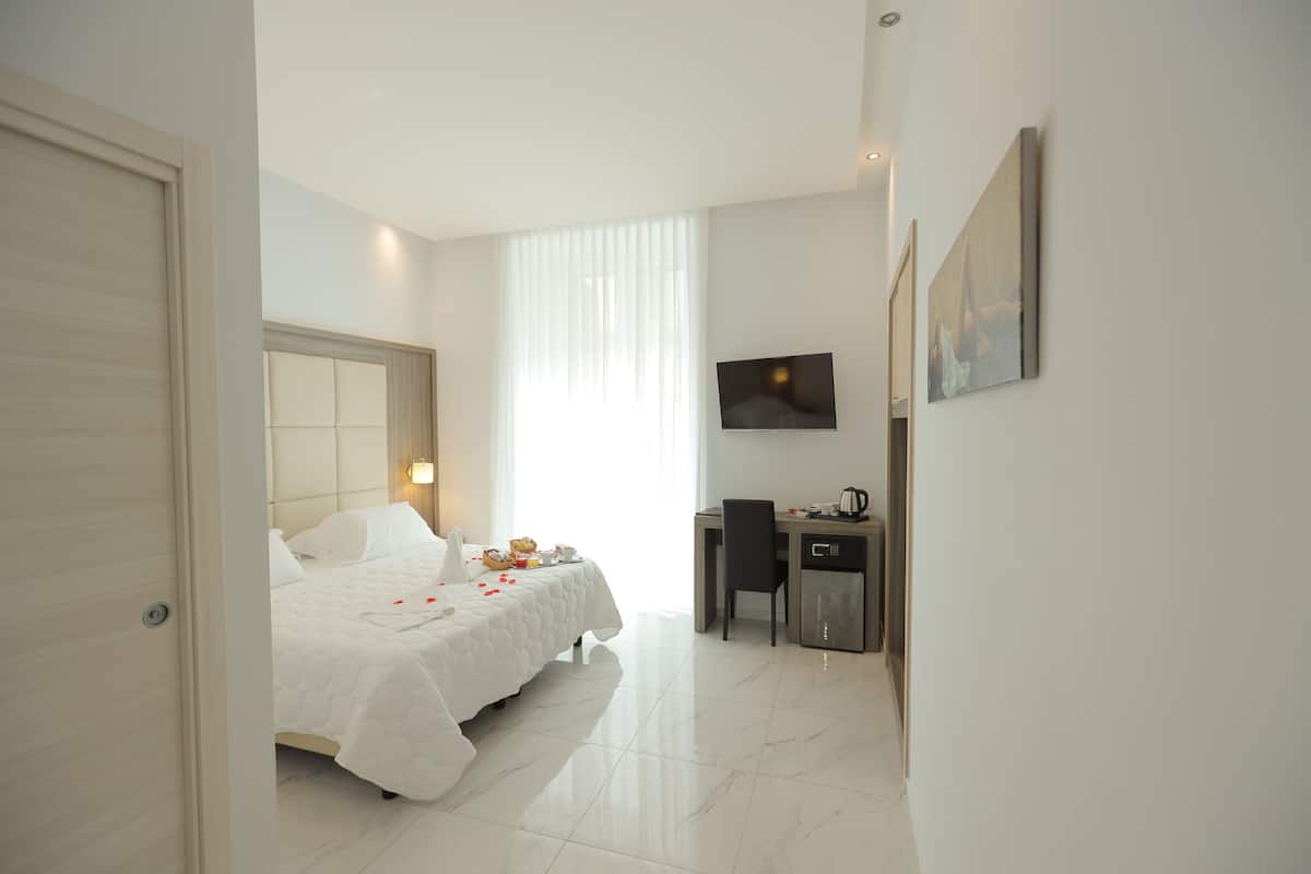 A hotel room with a bed, a desk, a chair, a television, and a door.