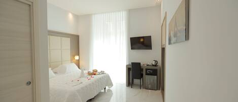 A hotel room with a bed, a desk, a chair, a television, and a door.