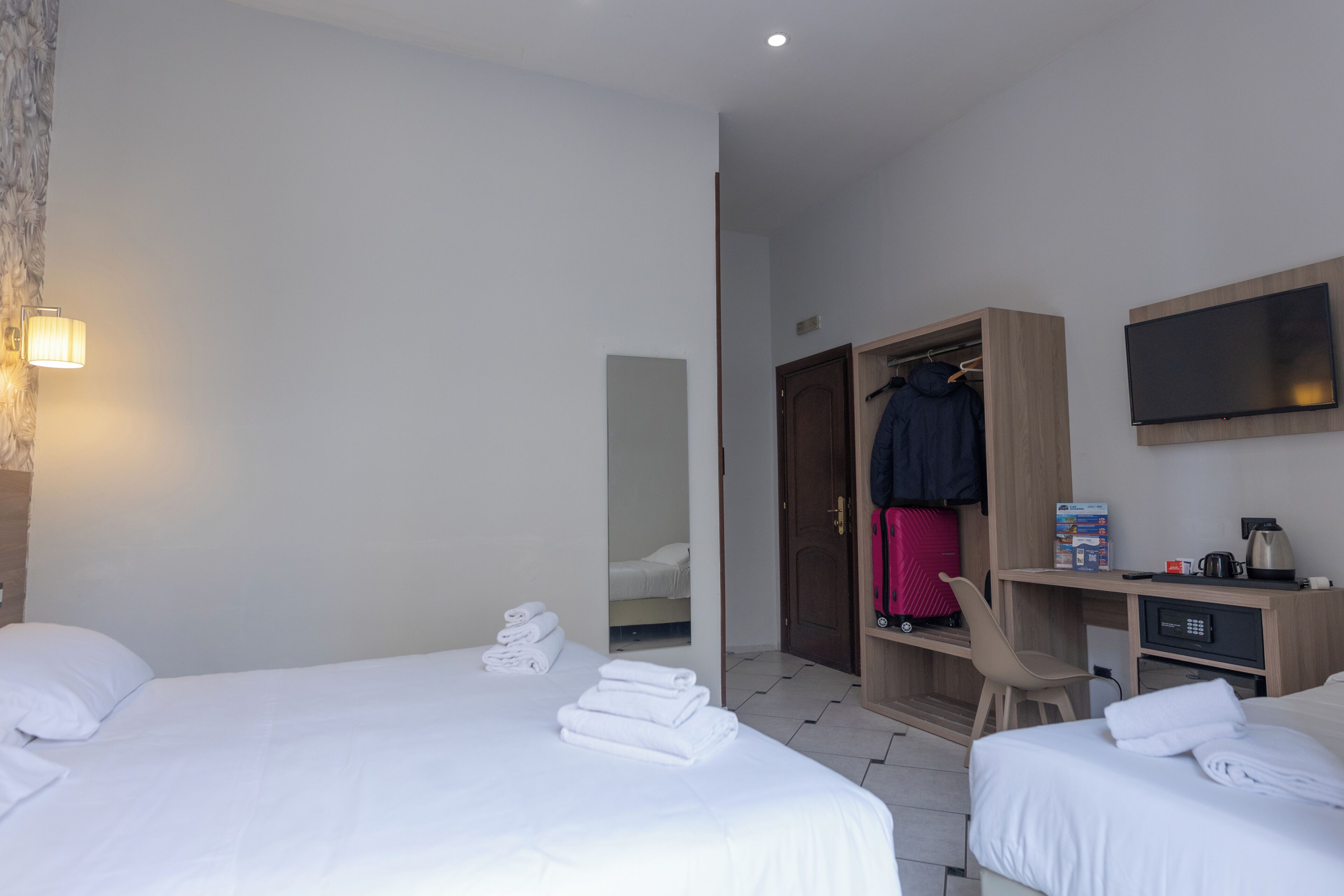 A hotel room with two beds, a desk, a wardrobe, a mirror, and a television.