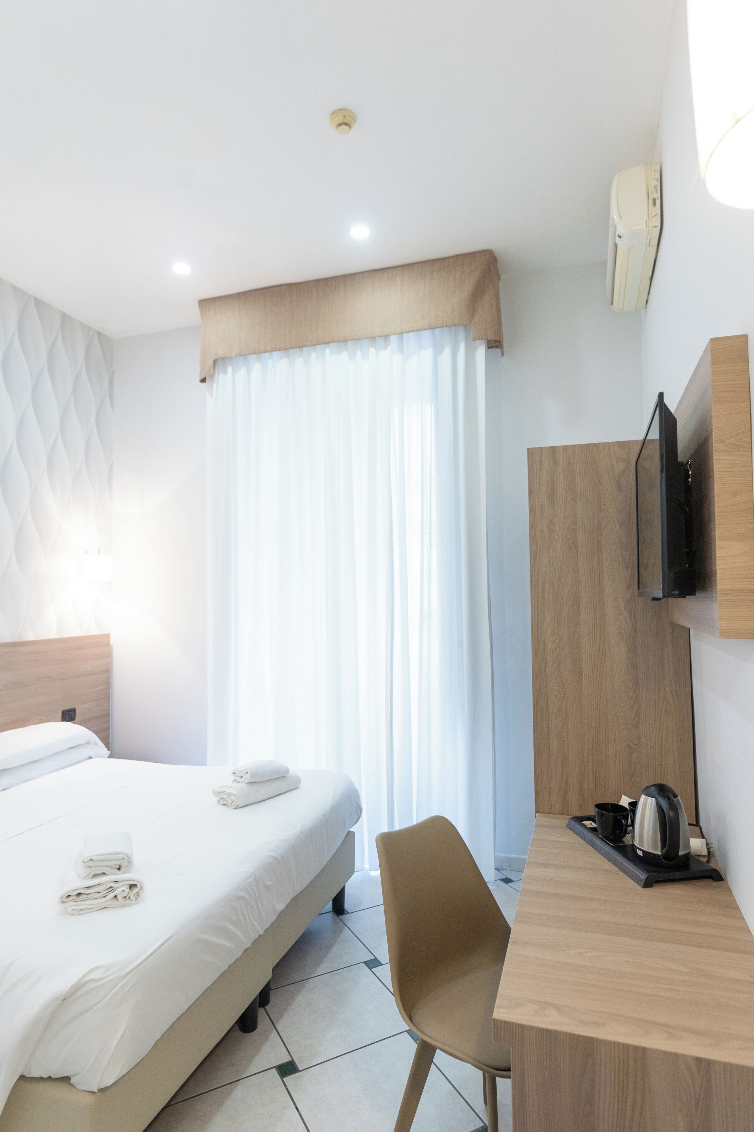 A hotel room with a bed, a desk, a chair, a television, and a window with curtains.