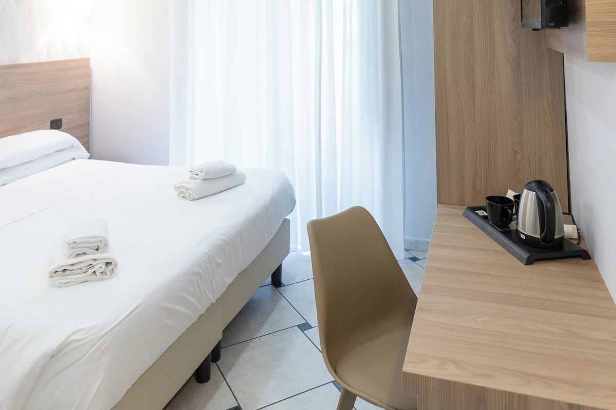 Ein Hotelzimmer mit Bett, Schreibtisch, Stuhl, Fernseher und einem Fenster mit Vorhängen.