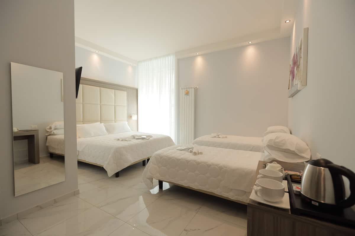A hotel room with two beds, a bedside table with a kettle, cups, and a tray of food.