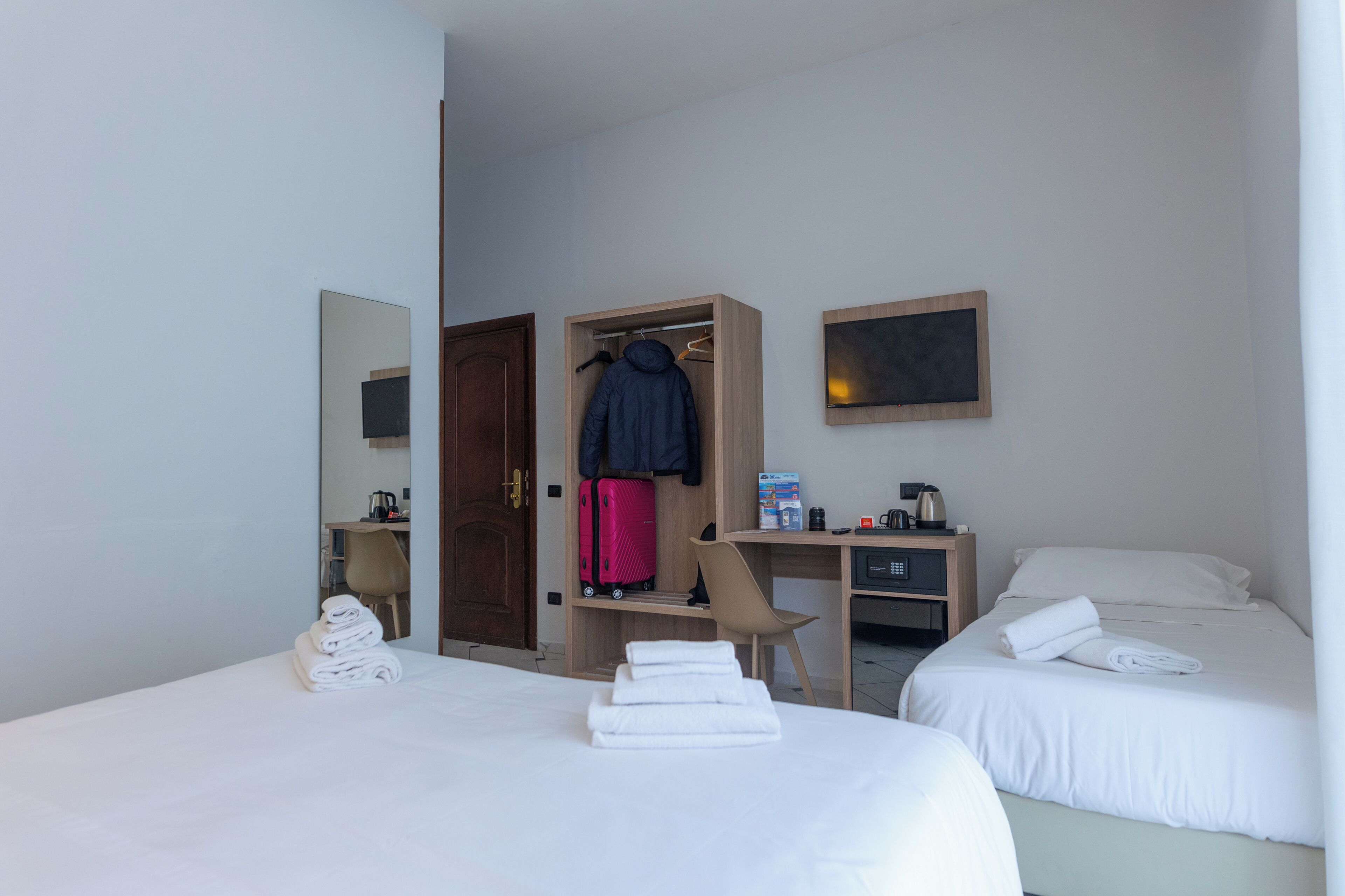 A hotel room with two beds, a desk with a computer, a wardrobe, and a mirror.