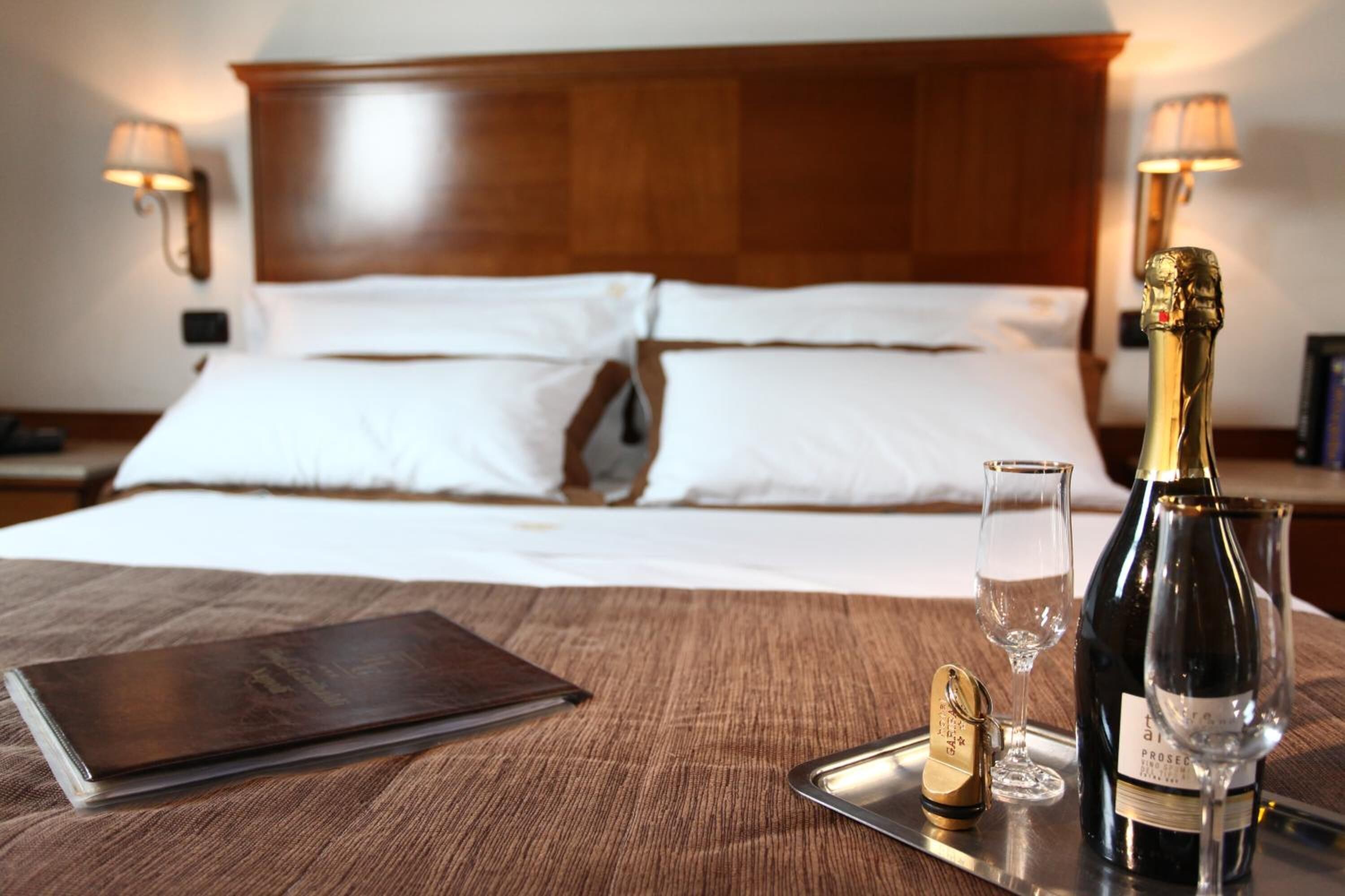 Un lit bien fait, avec du linge de lit blanc, une table de chevet sur laquelle se trouvent une bouteille de champagne, un verre et un plateau avec un tire-bouchon.