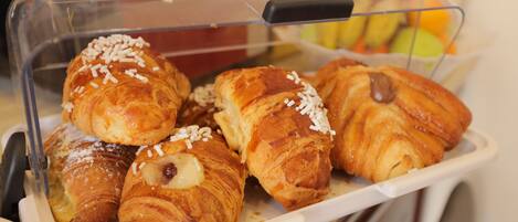 Una bandeja con una variedad de pasteles, incluyendo croissants y productos bañados en chocolate, en un recipiente de plástico transparente.