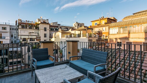 A rooftop terrace with outdoor furniture, a stone table, and a view of surrounding buildings. - President Gardens (Rome)