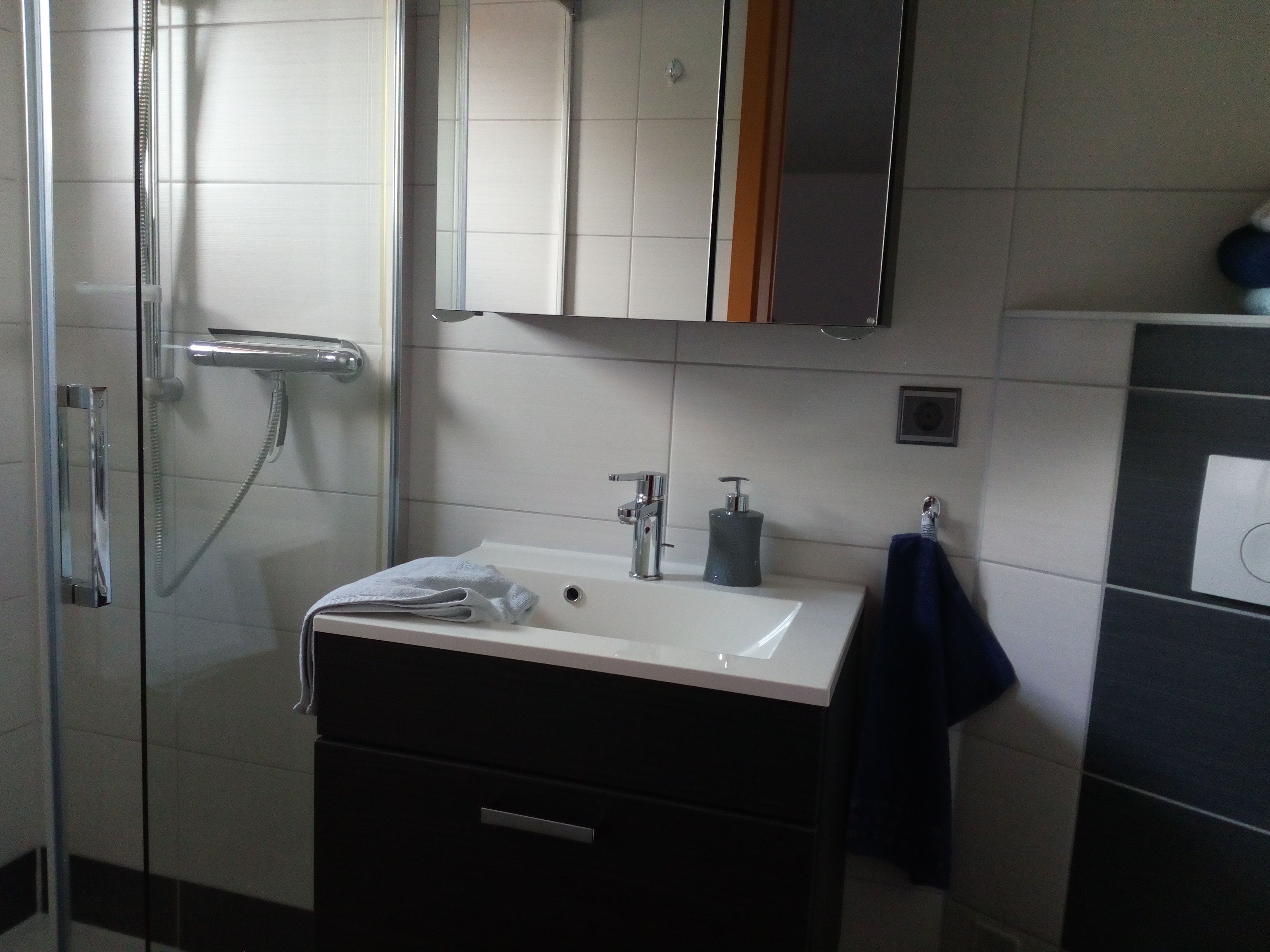 Un baño moderno con cabina de ducha de vidrio, un lavabo blanco con mueble oscuro y un espejo sobre el lavabo.