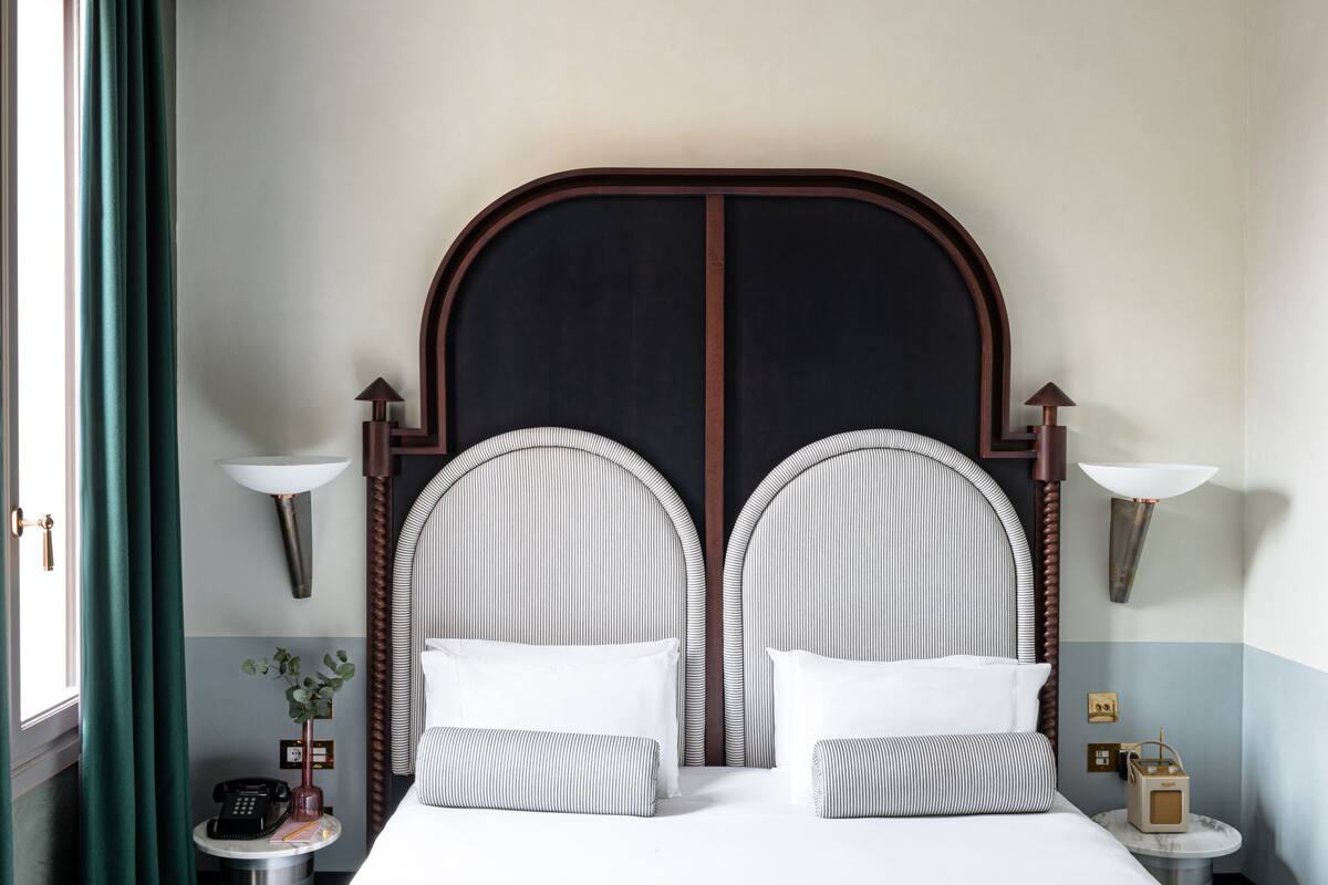 A double bed with a dark headboard, two bedside lamps, a small table with a telephone and a vase of flowers, and a nightstand with a lamp.