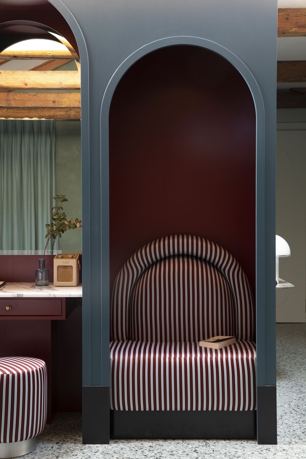 A cozy seating area with a striped chair and ottoman, a wooden desk with a radio, and a mirror reflecting a green curtain.