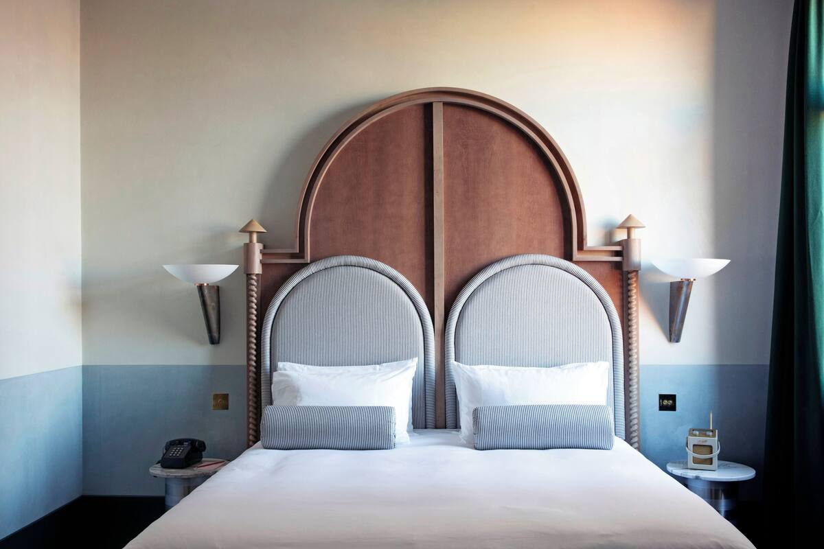 A hotel room with a large bed, two wall-mounted lamps, a bedside table with a phone, and a small table with a radio.