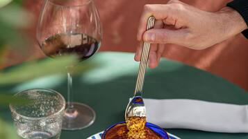 A dessert in a blue bowl on a striped plate, a wine glass, and a spoon on a table.