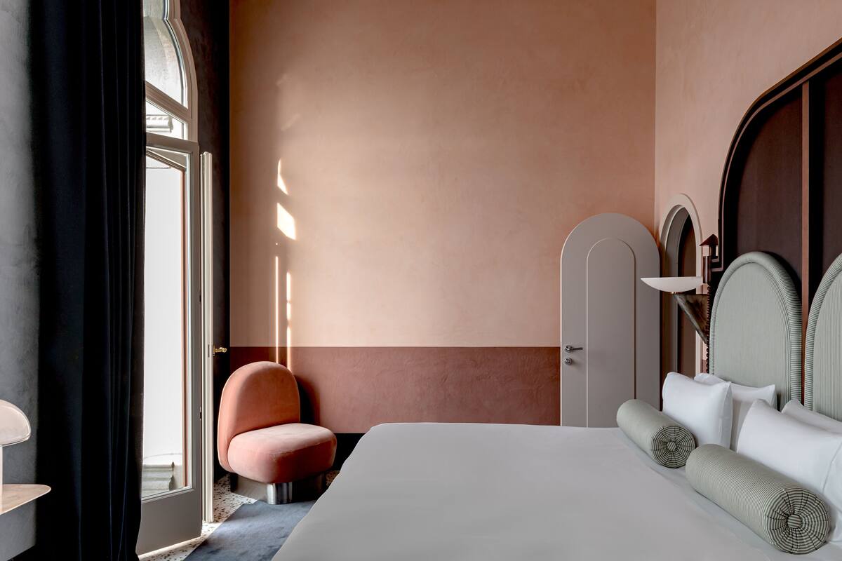 A hotel room with a bed, a chair, a wardrobe, and a door.