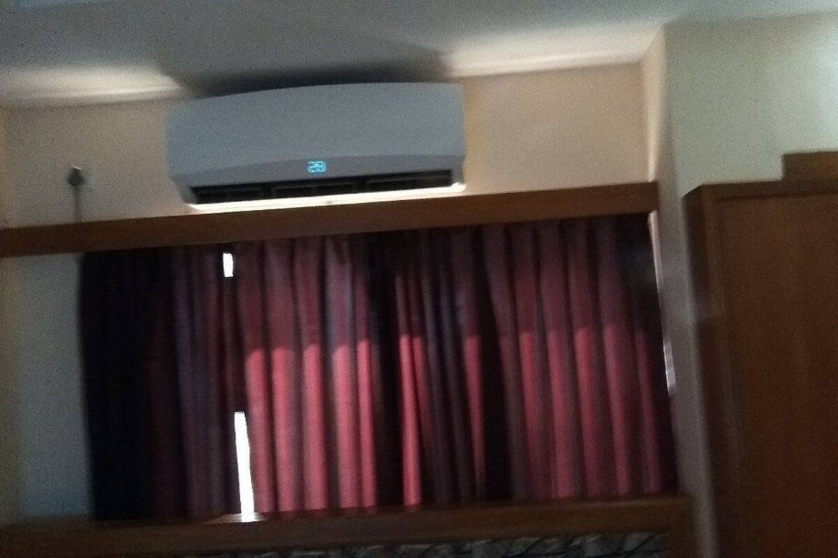 A room with a ceiling-mounted air conditioner, a window with red curtains, and a wooden door.