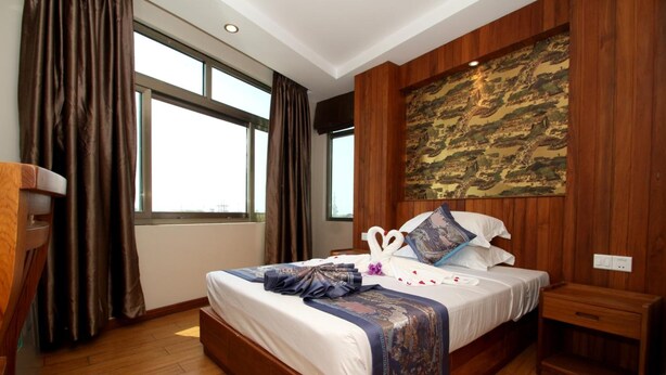 Habitación de hotel con una cama grande, paneles de madera, un ventanal amplio y una obra de arte tradicional en la pared.