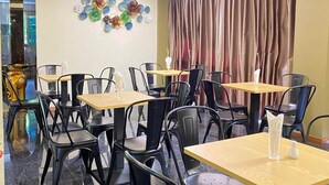 Un restaurante con varias mesas y sillas, un muro decorativo y un amplio ventanal con cortinas.