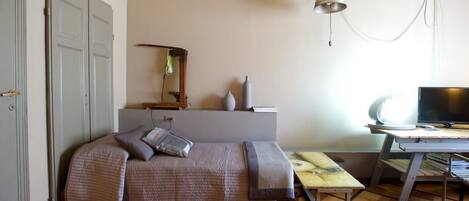 A compact bedroom with a bed, a desk, and a television.