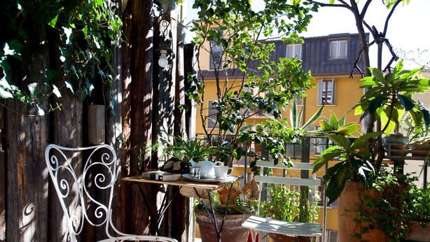 A balcony with a white metal chair, a small table with a cup and saucer, and several potted plants. - Bed più Art (Milan)