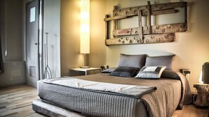 A bedroom with a large bed, a wooden headboard, a wall-mounted mirror, and a bedside table with a lamp. - Bed più Art (Milan)