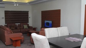 A modern living room with a sofa set, a coffee table, and a TV mounted on a brick wall. - Vulcan Suites (Abuja)