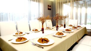 A dining table set for a meal with white chairs, a tablecloth, and a vase with dried flowers. - Villa Heaven Hills (Balchik)