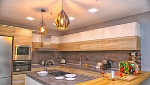 A modern kitchen with wooden cabinets, stainless steel appliances, a central island with a sink, and a hanging pendant light. - Villa Heaven Hills (Balchik)