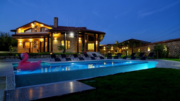 A swimming pool with lounge chairs and a flamingo float, surrounded by a house with stone walls and a tiled roof. - Villa Heaven Hills (Balchik)