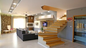 A modern living room with a staircase, a TV, and a stone wall. - Villa Heaven Hills (Balchik)