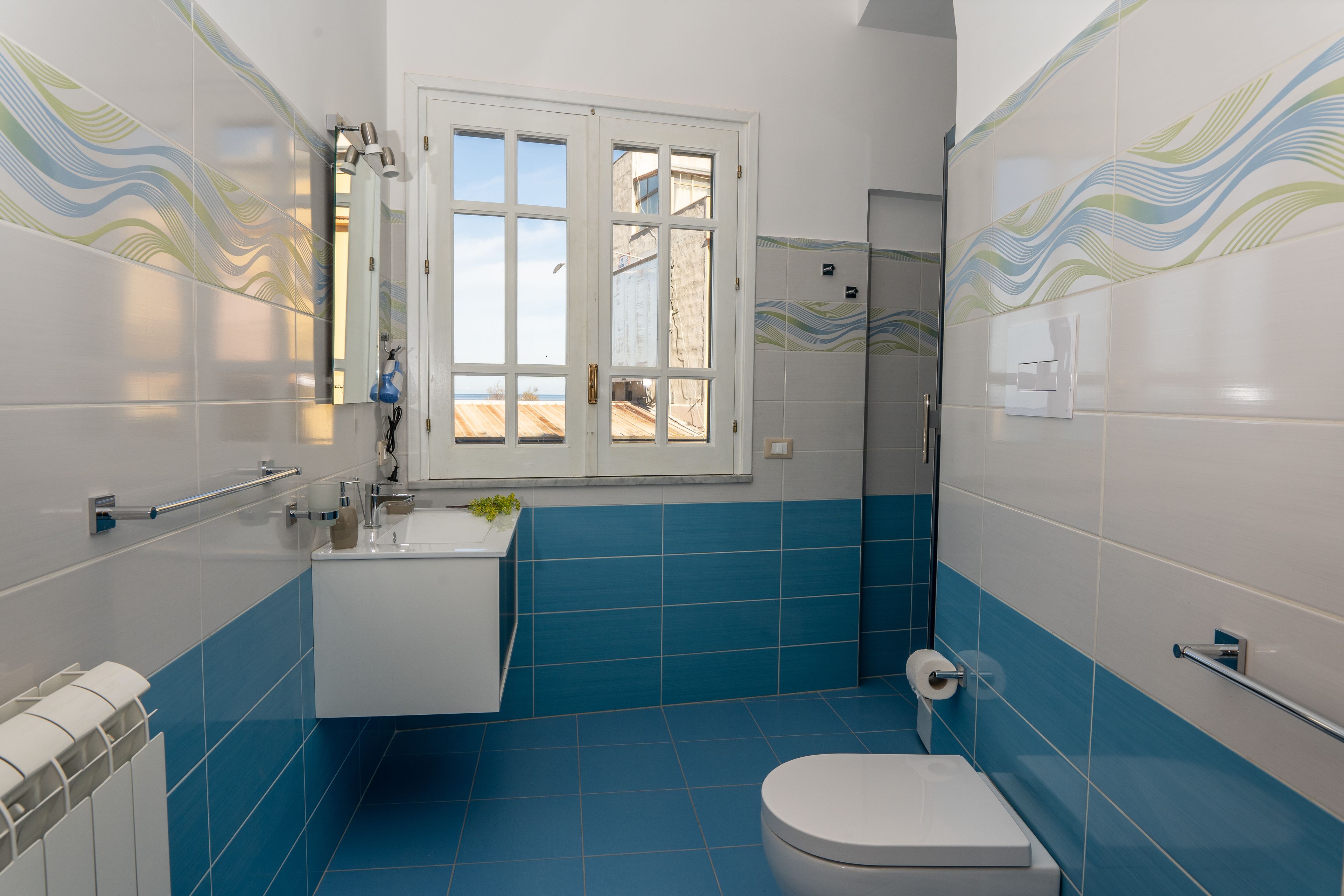 A bathroom with blue tiles, a white toilet, a sink, and a window.