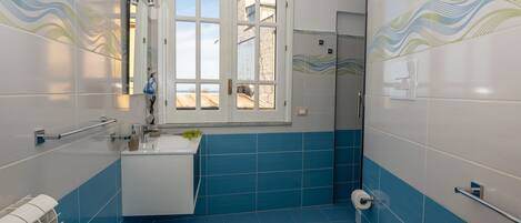A bathroom with blue tiles, a white toilet, a sink, and a window.