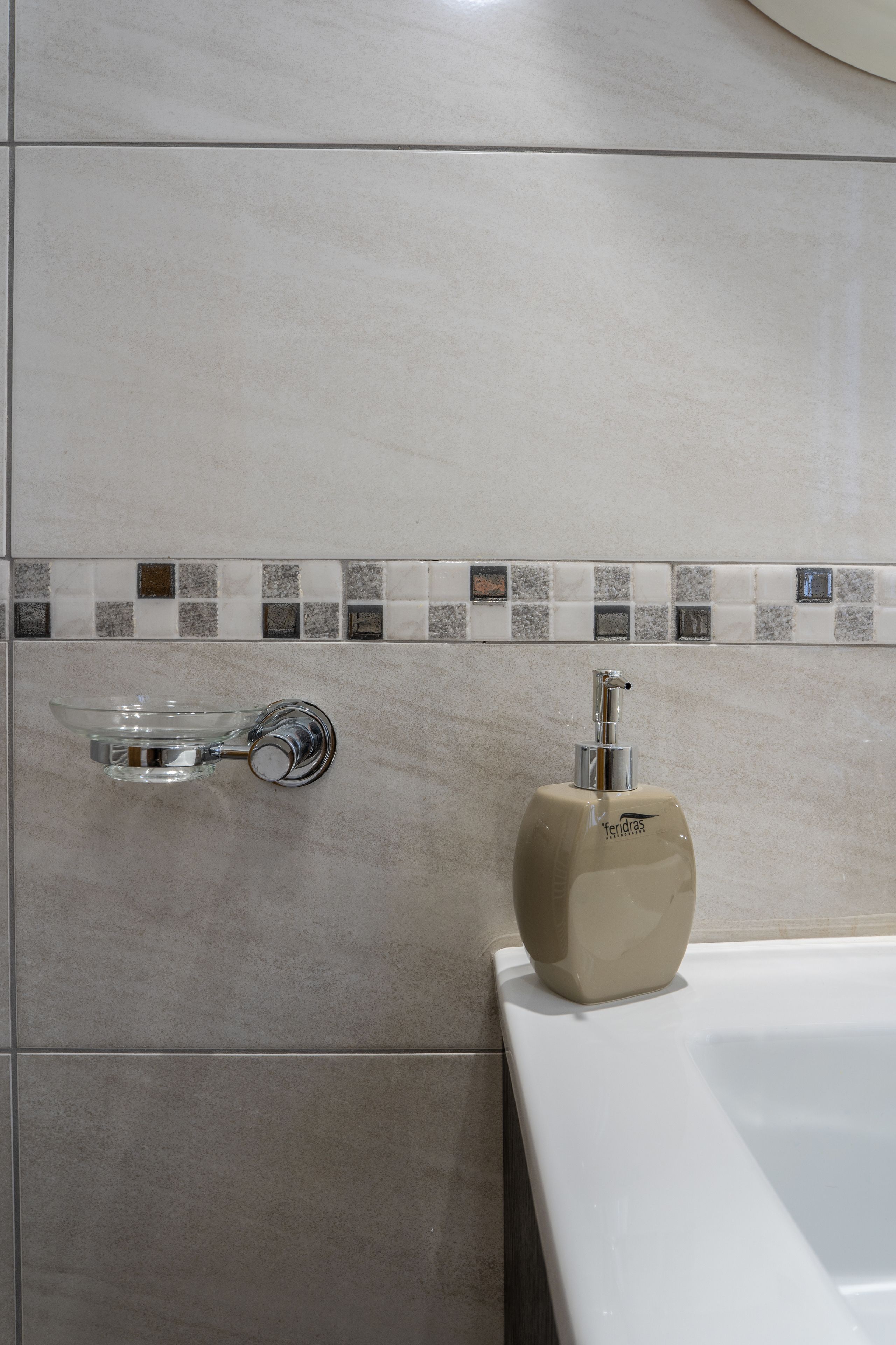 A bathroom with a glass soap dish, a beige soap dispenser, and a tiled backsplash.