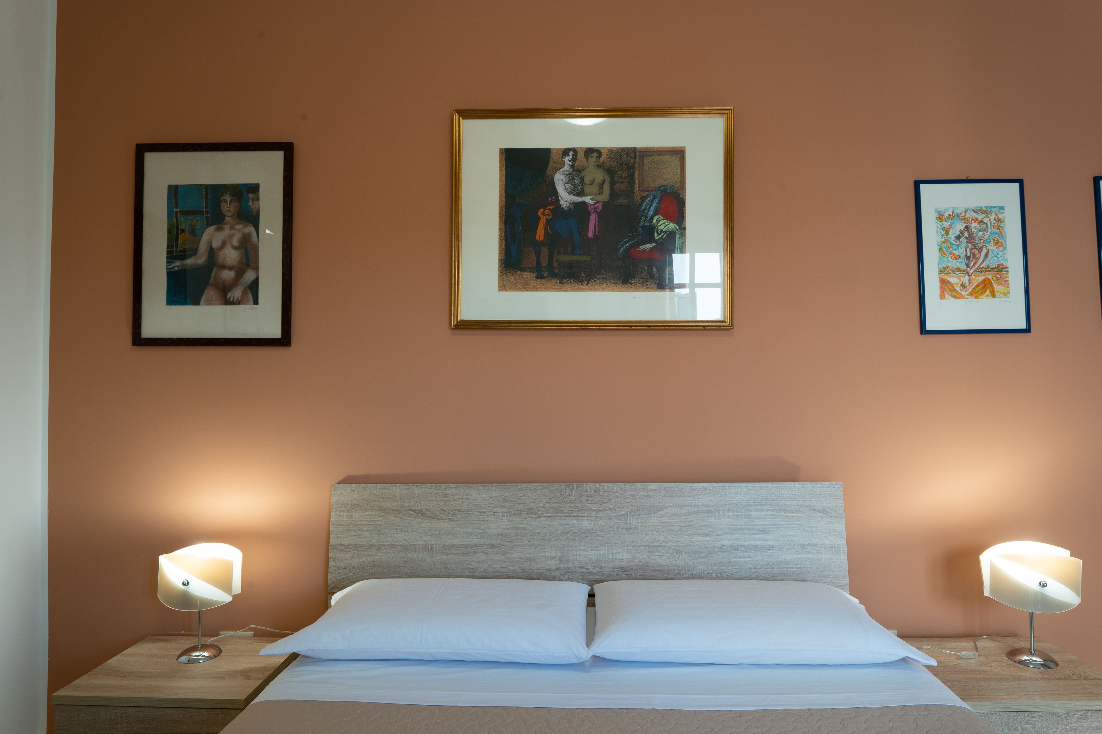 A bedroom with a bed, two bedside tables, and three framed artworks on the wall.