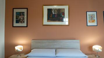 A bedroom with a bed, two bedside tables, and three framed artworks on the wall.