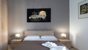 A neatly made bed with a dark quilt, two bedside tables with lamps, and a wall-mounted artwork of birds. - Una Terrazza sul Golfo (Palermo)