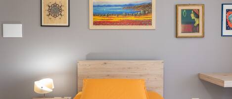 A bedroom with a wooden headboard, an orange pillow, a bedside lamp, and framed artwork on the wall.