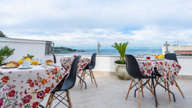 An outdoor dining area with tables covered in floral tablecloths, chairs, and a view of the sea. - Una Terrazza sul Golfo (Palermo)