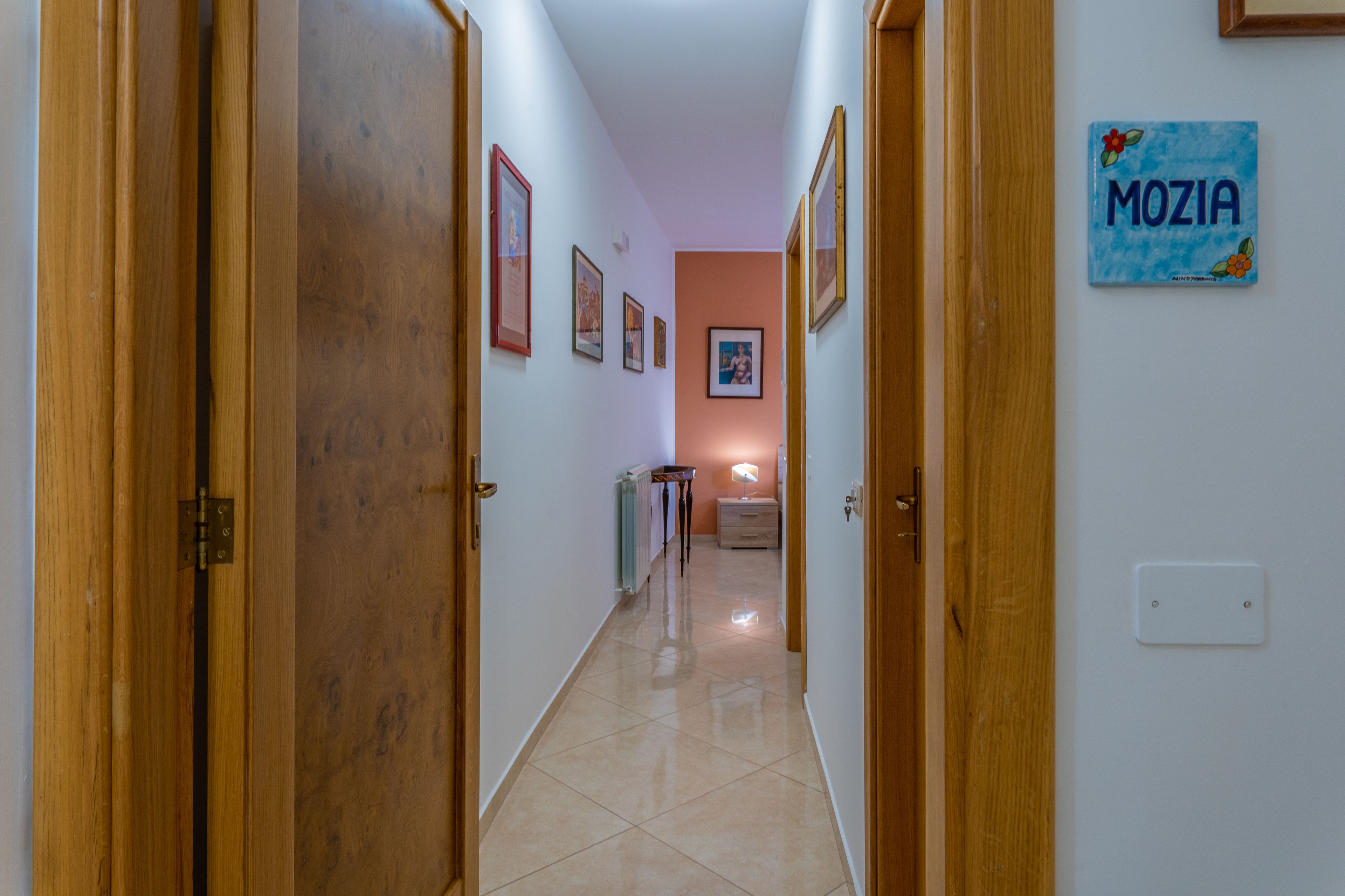 Un passadís amb portes de fusta, quadres a les parets i un rètol que diu "MOZIA".