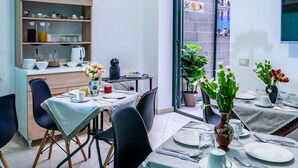 A modern dining area with a table set for four, a wooden shelf with kitchenware, and a potted plant. - Una Terrazza sul Golfo (Palermo)