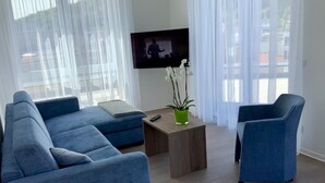 Uma sala de estar moderna com um sofá azul, uma poltrona combinando, uma mesa de centro e uma TV fixada na parede.