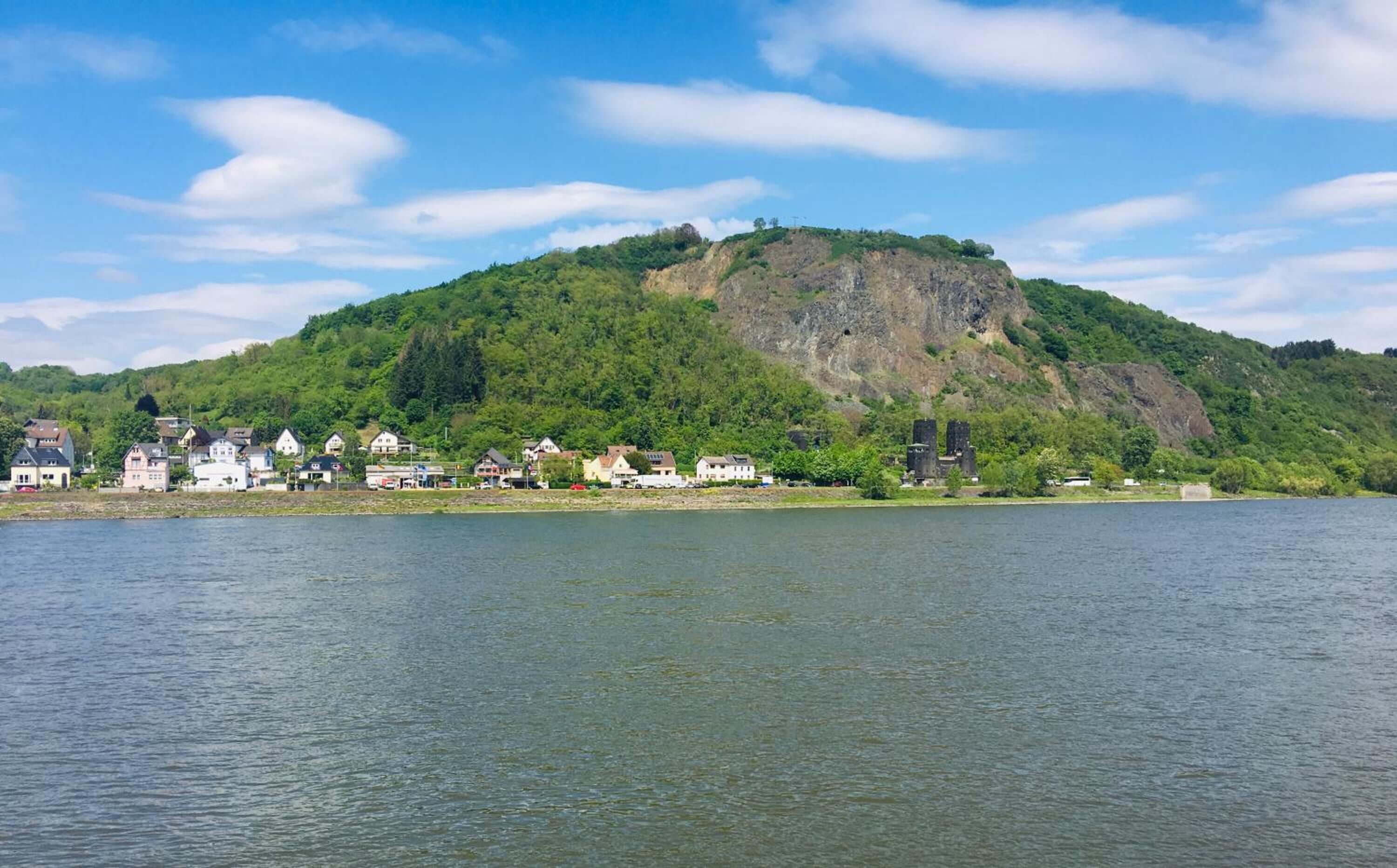 A lakeside town with houses along the shore and a hill with a castle-like structure in the background.