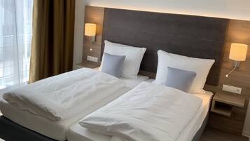 Un lit double avec du linge de lit blanc et deux oreillers, une tête de lit en bois, des lampes de chevet et une table de chevet avec une lampe.